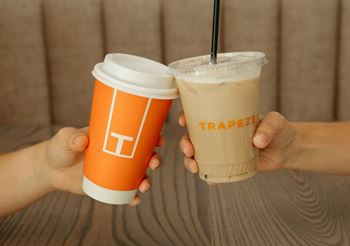 person holding two coffee cups in their hands in front of a wooden table